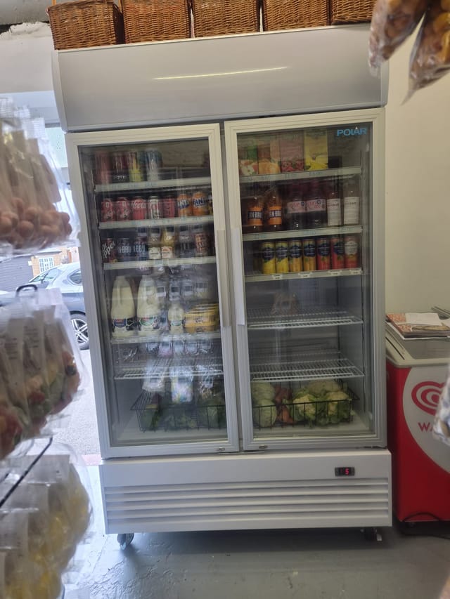 The drinks fridge, stocked with soft drinks, juice, milk and fresh vegetables